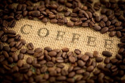 Coffee beans surrounding the word coffee stamped on burlap sack
