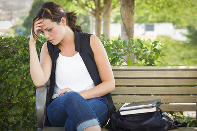 Upset Young Woman Sitting Alone with Her Head in Her Hands on Bench Next to Books and Backpack.